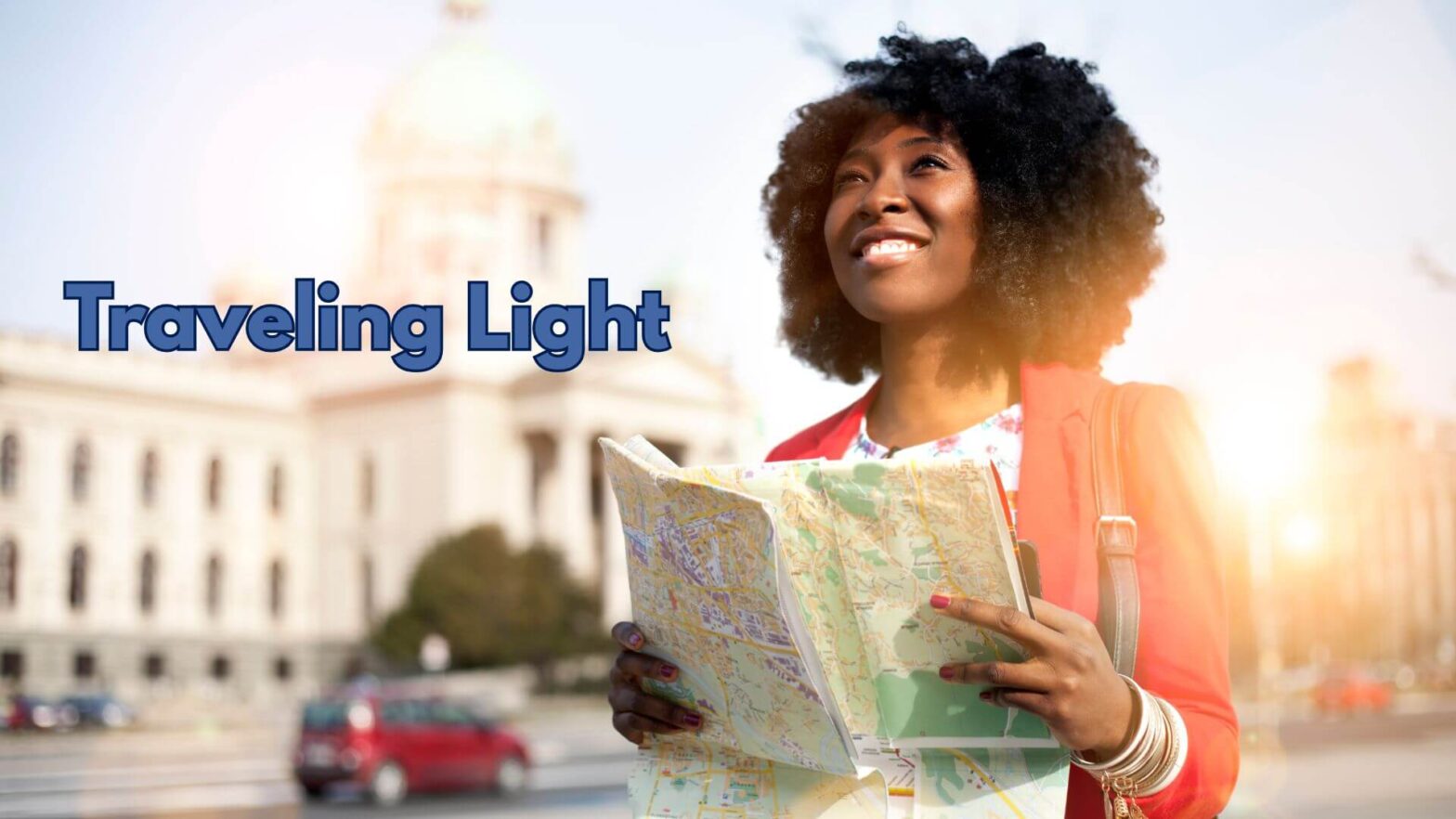 Women smiling and holding a map with the sun behind her and a building in the background. The words traveling light appear on the left side.